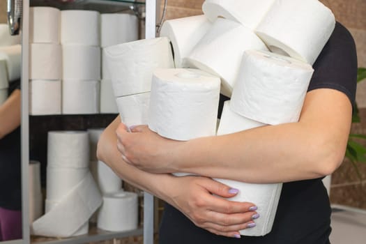 People are stocking up toilet paper for home quarantine from coronavirus. Woman holds many rolls of toilet paper.