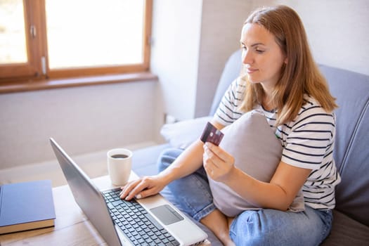 Beautiful carefree woman holding credit card and using laptop computer. Online shopping, e-commerce, internet banking, spending money, working from home concept. Businesswoman working at home.