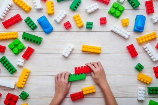 Baby hands playing with colorful plastic blocks on white wooden table background. Developing toys. Learning by playing.