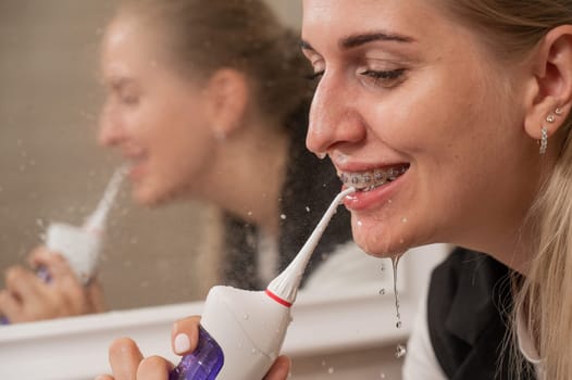 A woman with braces on her teeth uses an irrigator. Close-up portrait