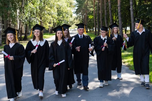 A group of graduates in robes with diplomas in their hands walk outdoors. Elderly student