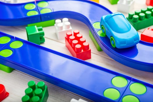 Baby kid toys background. Toy car, plastic road and colorful blocks on white wooden background.