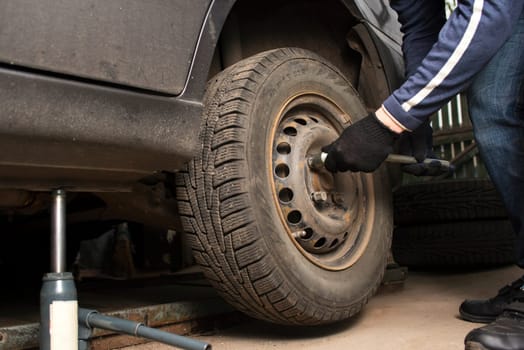 Auto mechanic tightening the nuts with a wheel wrench. Seasonal tire change. Car service concept