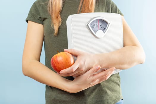A woman holding weight scales and red apple on a blue background. Healthy eating concept. Diet.