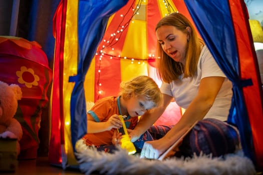 Happy loving family. Young mother and her son boy play in children room at the bedtime. Mom and lovely child are having fun with flashlights indoors. Family concept.