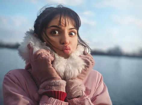 Portrait of a cute lady with a kiss, with bangs, in a pink jacket on the background of the river.