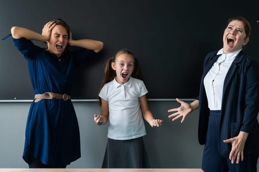Female teacher, schoolgirl and her mother yell at each other while standing at the blackboard