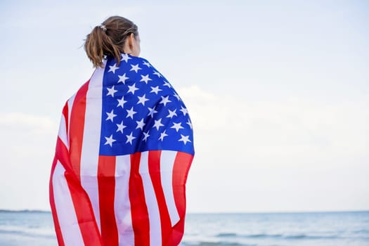 Back view of young woman holding national American flag on a ocean beach. USA Memorial day and Independence day concept.