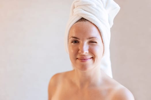 Portrait of a cheerful attractive woman with a towel wrapped around her head winking and looking at camera, afrer beauty treatments.