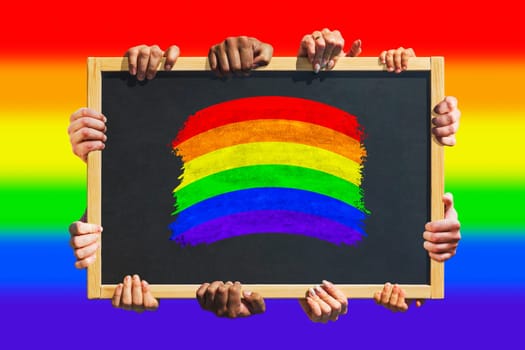 A lot of hands are holding a poster with LGBT flag - symbol of love and tolerance. Lesbian, Gay, Bisexual and Transgender rights. Concept of the Pride day.