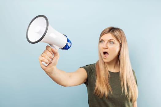 Young blonde woman shouting loudly while holding a megaphone on blue background. Concept of speech and announce, idea for marketing or sales.