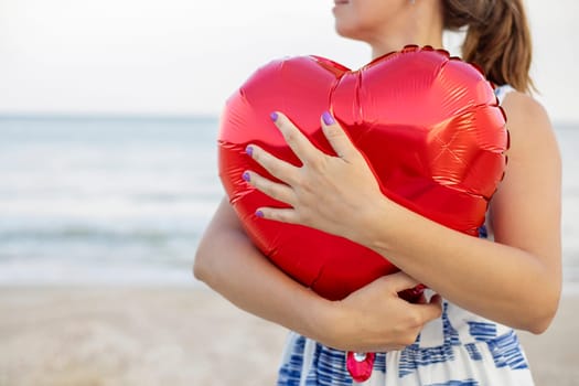 Happy young woman huging heart-shaped balloon on the beach.