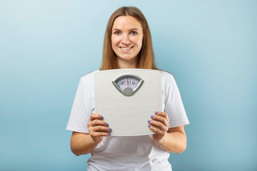 Young woman holding white scales to check the results of her diet . Diet and sport concept.