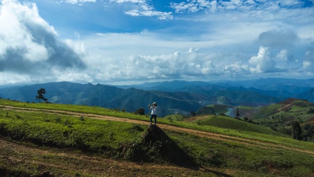 Tourists stand on the rocks enjoying the picturesque hillside views with vast fields on a beautiful sunny day with blue sky and clouds in springtime.