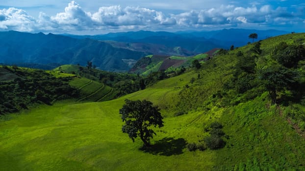 Scenic of idyllic rolling hills landscape with blooming meadows and mountain ranges in the background on a beautiful sunny day with blue sky and clouds in springtime.