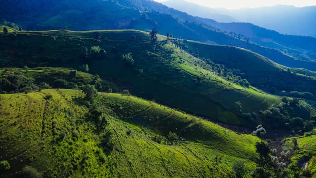 Scenic of idyllic rolling hills landscape with blooming meadows and mountain ranges in the background on a beautiful sunny day with blue sky and clouds in springtime.