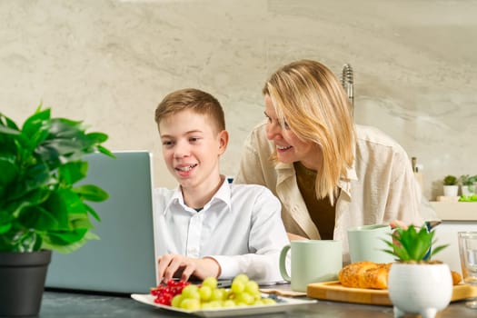 Happy mother and son have healthy breakfast in the kitchen at home. Happy mother and son in the kitchen. breakfast and digital devices Concept of happy family and healthy food.