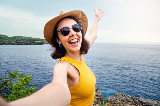 Young woman traveler wearing hat and sunglasses taking selfie in Nusa Penida, Bali. Female taking picture in summer vacation. Copy space. Travel, freedom and happiness concept.