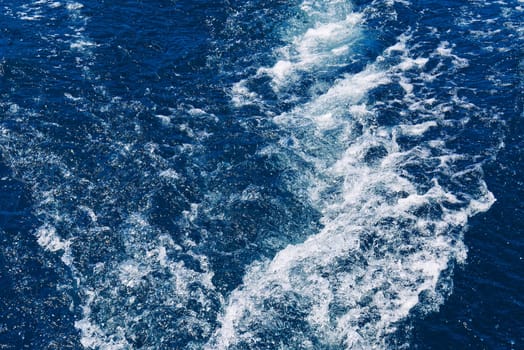 Abstract blue sea water with white waves. Blue sea texture with waves and foam. Rough deep turquoise and blue Mediterranean sea. Sea water top view.