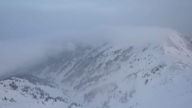 Mystical dawn with clouds in snowy mountains. The white hills are covered with clouds and snow. Steep rocky cliffs. The high peaks of the peaks. The rays of the sun at dawn pass through the clouds