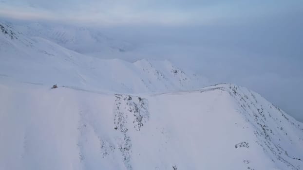 Mystical dawn with clouds in snowy mountains. The white hills are covered with clouds and snow. Steep rocky cliffs. The high peaks of the peaks. The rays of the sun at dawn pass through the clouds