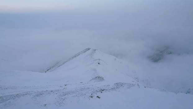 Mystical dawn with clouds in snowy mountains. The white hills are covered with clouds and snow. Steep rocky cliffs. The high peaks of the peaks. The rays of the sun at dawn pass through the clouds