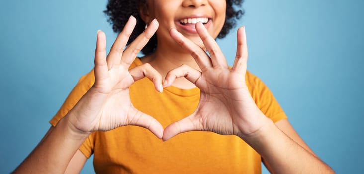 Happy, hand and closeup of a heart shape for romance, care or flirting expression in a studio. Happiness, positive and zoom of a woman with a love gesture, emoji or sign isolated by a blue background.