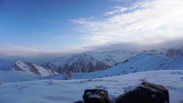 An ocean of clouds in the snowy mountains at dawn. White clouds are like a carpet in a gorge. Waves rise and descend from the mountains. Sunrise of the yellow sun. There are stones lying. Kazakhstan