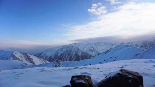 An ocean of clouds in the snowy mountains at dawn. White clouds are like a carpet in a gorge. Waves rise and descend from the mountains. Sunrise of the yellow sun. There are stones lying. Kazakhstan