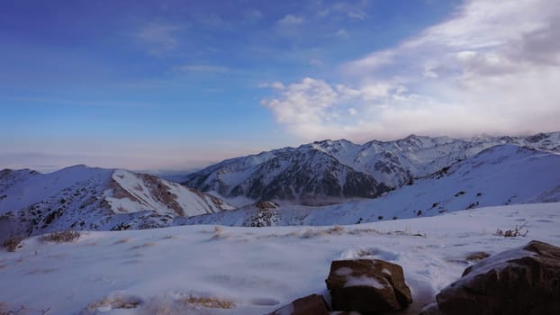 An ocean of clouds in the snowy mountains at dawn. White clouds are like a carpet in a gorge. Waves rise and descend from the mountains. Sunrise of the yellow sun. There are stones lying. Kazakhstan