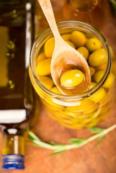 Close up green olives in bank, rosemary on a wooden background