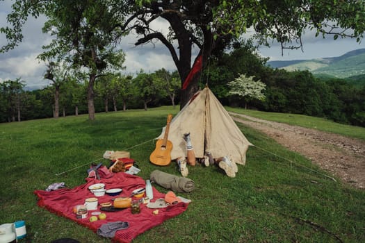 Family on vacation with a tent in the forest. Picnic in nature. People are lying down, resting. The legs are visible from the tent. Acoustic guitar.