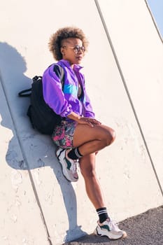 vertical photo of an african american young woman in sports clothes leaning on an urban wall, concept of active lifestyle and urban sport