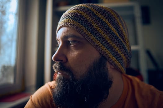 A man with a beard wearing a striped hat and t-shirt, looking up into the window