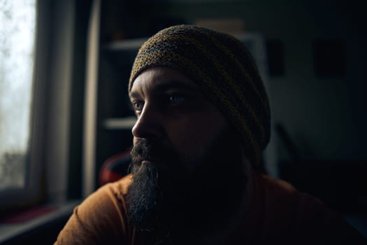 A man with a beard wearing a striped hat and t-shirt, looking up into the window