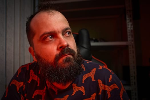 Portrait of an adult male with a beard, works in front of a computer, mixed color light, indoor