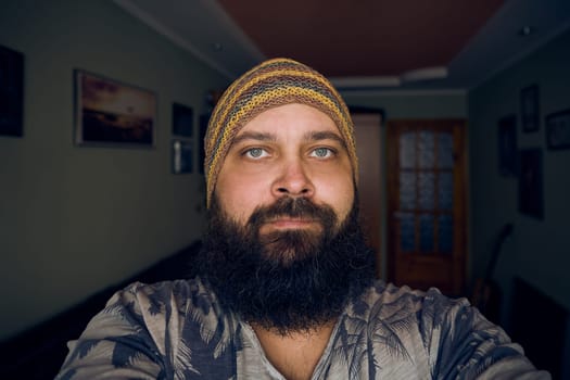 A man with a beard wearing a striped hat and shirt, looking up into the camera