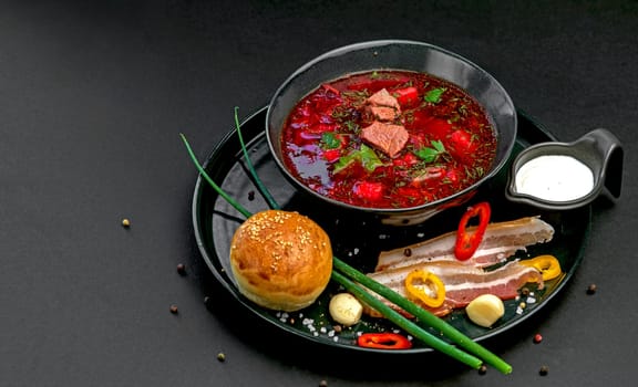Ukrainian borsch. Beetroot soup. Ukrainian cuisine.In a wooden plate with salted bacon, bread and herbs. On dark background. The view from the top. Free space for your text. A bowl of red beet soup