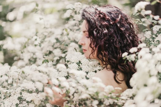 Woman spirea flowers. Portrait of a curly happy woman in a flowering bush with white spirea flowers