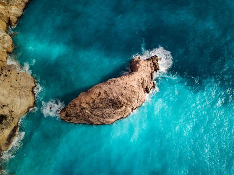 Aerial views of the turquoise sea water with wild seashore and waves reaching steeply rocks on a sunny day. 