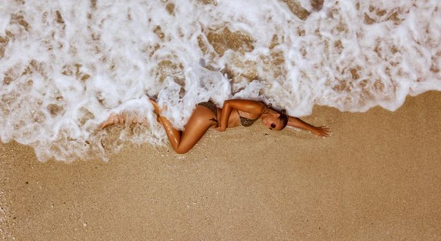 Top view of a beautiful young woman enjoying in sunbath on the beach in a bikini, relaxing in summer tropical clear sea waves.