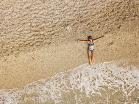 Top view of a beautiful woman enjoying in sunbath on the beach in a bikini, relaxing near summer tropical clear sea waves.