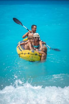 Happy family is enjoying paddling in yellow kayak at tropical ocean water during summer vacation.They are kayaking on the sea.