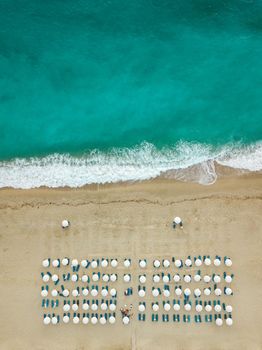 Aerial view of the amazing idyllic empty beach with white umbrellas and blue sunbed.