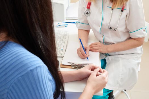 Cropped image of Young smart doctor diagnosing and giving advice to his patient while sitting together at the doctor working desk