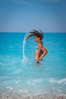 Joyful little girl flips her long hair out of sea and splashes water high in the air.