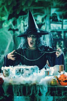 Witch with awfully face and hat on her head in creepy surroundings full of cobweb sends evil. Halloween concept.