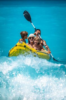 Happy family is enjoying paddling in yellow kayak at tropical ocean water during summer vacation.They are kayaking on the sea.