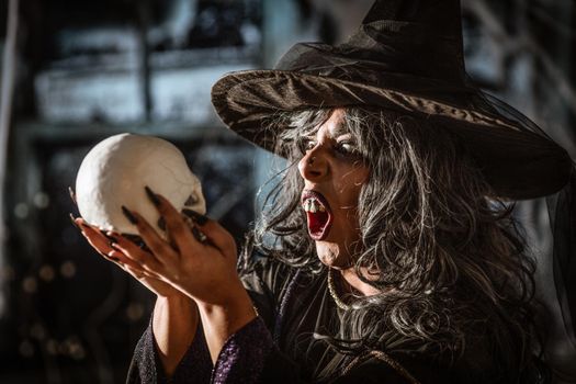 Portrait of witch with awfully face in creepy surroundings and smoky green background talks with dead. Halloween concept.