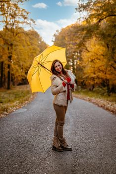 Beautiful cheerful young woman with yelow umbrella having fun in sunny park in autumn colors.